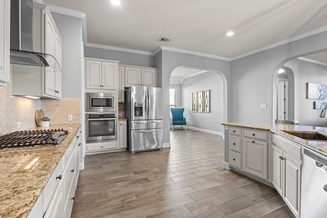 kitchen featuring wall chimney exhaust hood, light stone counters, white cabinets, and stainless steel appliances