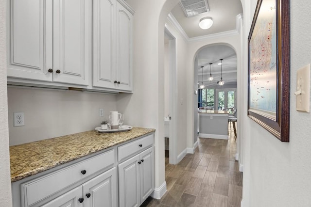 bar featuring white cabinets, dark hardwood / wood-style floors, light stone counters, and ornamental molding