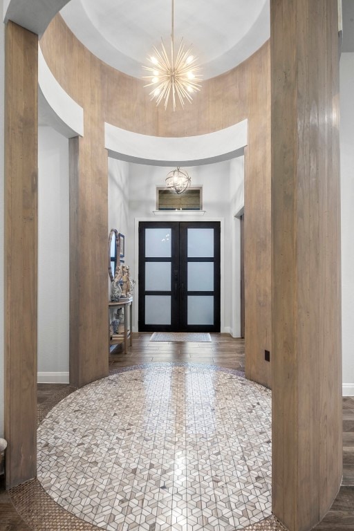 entryway featuring hardwood / wood-style flooring, a notable chandelier, wood walls, and french doors