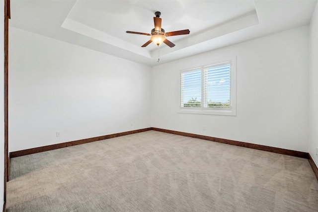 unfurnished room featuring ceiling fan, light carpet, and a tray ceiling