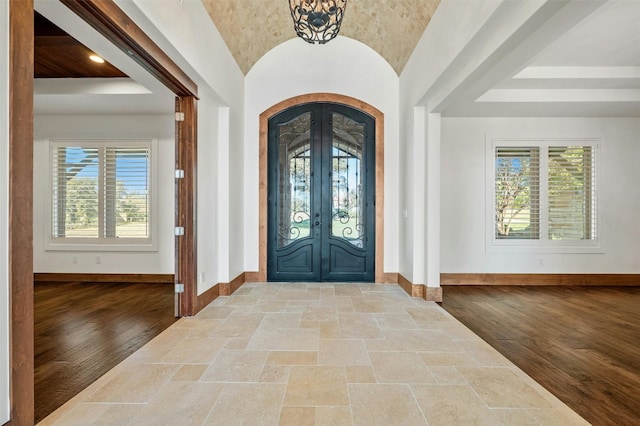 foyer featuring french doors, a chandelier, vaulted ceiling, and light wood-type flooring