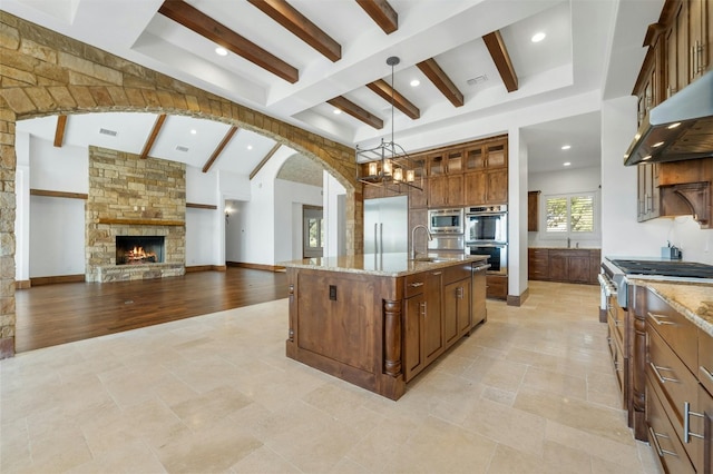 kitchen with pendant lighting, a kitchen island with sink, light hardwood / wood-style floors, light stone counters, and stainless steel appliances