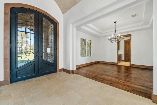 foyer entrance with french doors, a healthy amount of sunlight, a notable chandelier, and light wood-type flooring