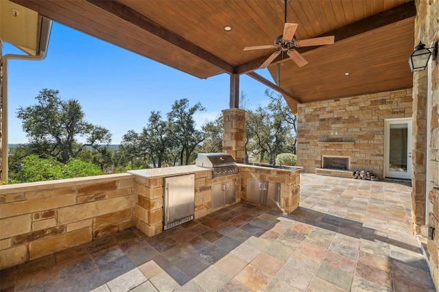 view of patio featuring ceiling fan, a grill, an outdoor stone fireplace, and exterior kitchen