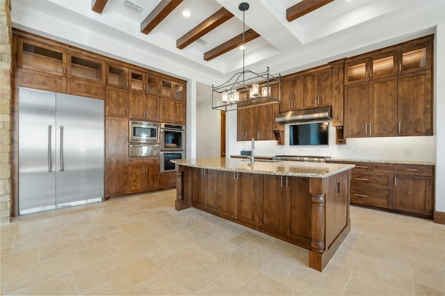 kitchen featuring light stone countertops, beam ceiling, built in appliances, decorative light fixtures, and an island with sink