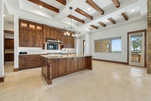 kitchen featuring beam ceiling, range hood, a notable chandelier, pendant lighting, and a kitchen island with sink