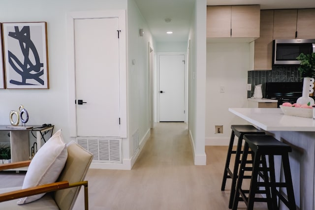 kitchen featuring decorative backsplash, black stove, light hardwood / wood-style floors, and a kitchen breakfast bar