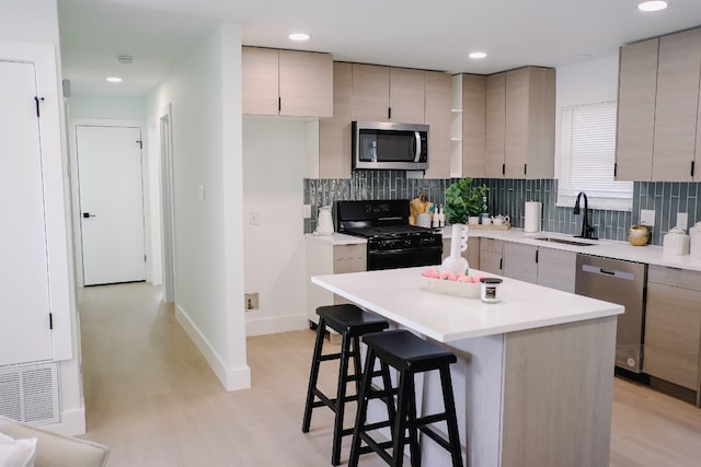 kitchen with sink, a center island, a breakfast bar area, appliances with stainless steel finishes, and light wood-type flooring