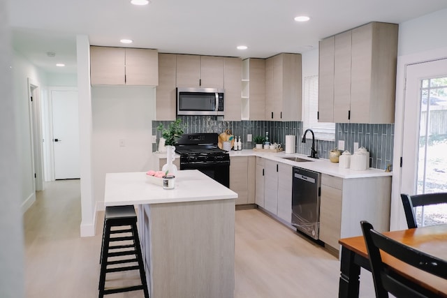 kitchen featuring sink, a kitchen island, appliances with stainless steel finishes, tasteful backsplash, and light hardwood / wood-style floors