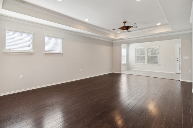 empty room with dark hardwood / wood-style flooring, a tray ceiling, ceiling fan, and crown molding