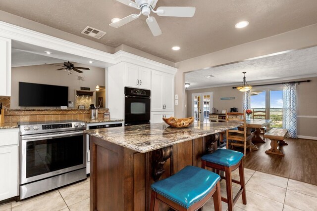 kitchen featuring white cabinetry, a center island, light tile patterned floors, oven, and stainless steel stove