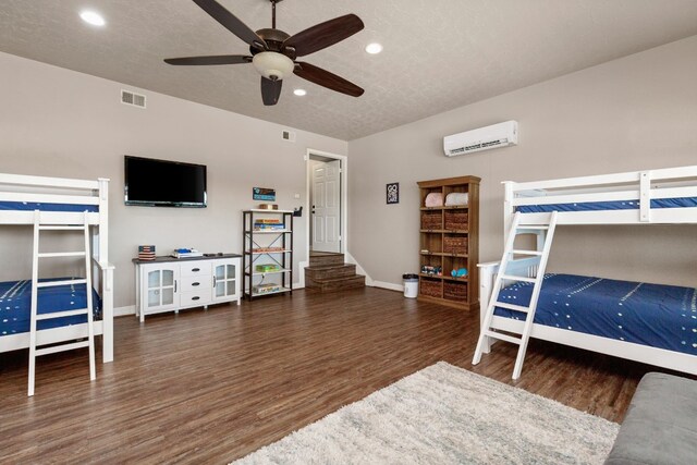 bedroom featuring a wall mounted air conditioner, a textured ceiling, dark hardwood / wood-style flooring, and ceiling fan