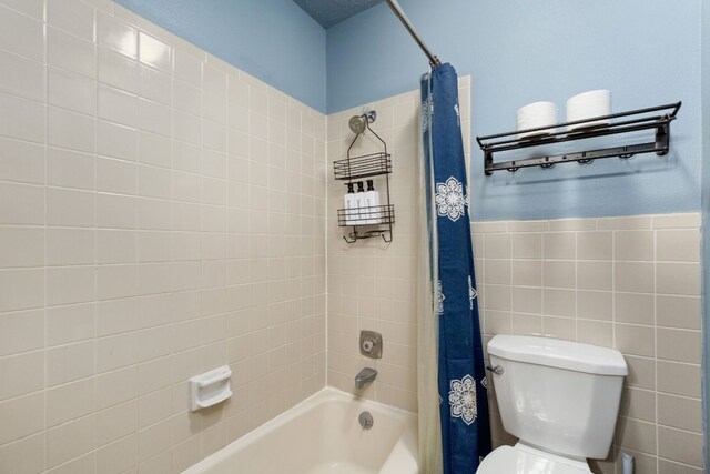 bathroom featuring toilet, shower / tub combo with curtain, and tile walls