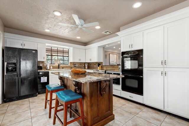 kitchen with decorative backsplash, light stone countertops, black appliances, white cabinets, and a kitchen island