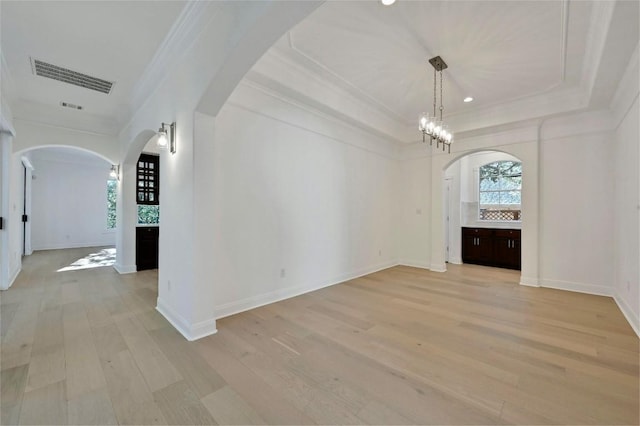 interior space with a raised ceiling, light wood-type flooring, an inviting chandelier, and crown molding