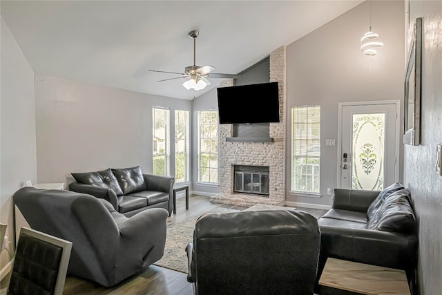 living room featuring ceiling fan, a stone fireplace, wood-type flooring, and high vaulted ceiling