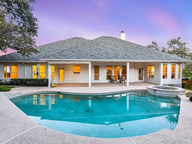 pool at dusk featuring a patio area and an in ground hot tub