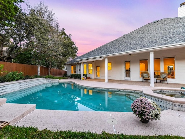 pool at dusk with an in ground hot tub and a patio area