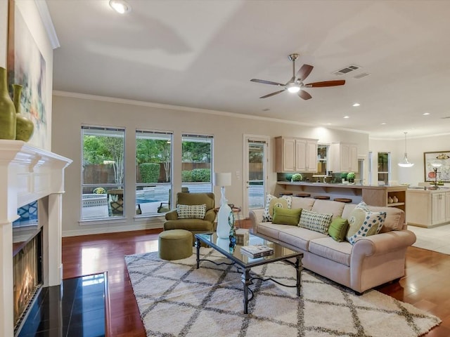 living room featuring ceiling fan, ornamental molding, and light wood-type flooring