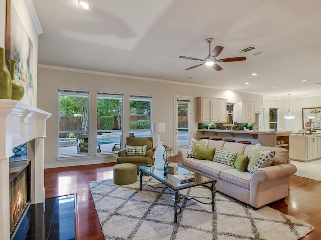 1624 Cabinwood Cv, Austin, TX 78746 - living room with crown molding, visible vents, a ceiling fan, wood finished floors, and a lit fireplace
