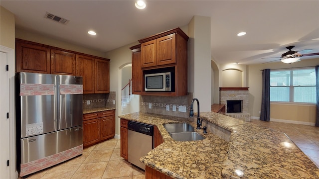 kitchen with decorative backsplash, appliances with stainless steel finishes, light stone counters, sink, and a fireplace