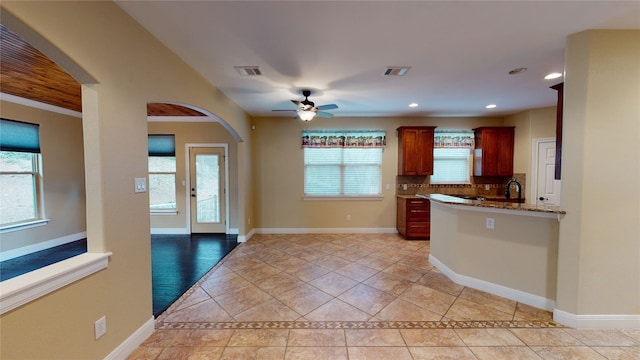 kitchen with light stone countertops, decorative backsplash, ornamental molding, ceiling fan, and light tile patterned floors