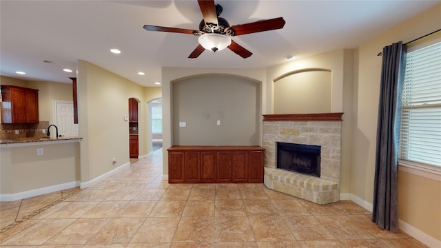 unfurnished living room with ceiling fan, light tile patterned flooring, sink, and a fireplace