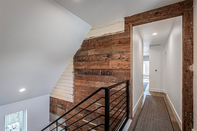 hall featuring vaulted ceiling and wooden walls