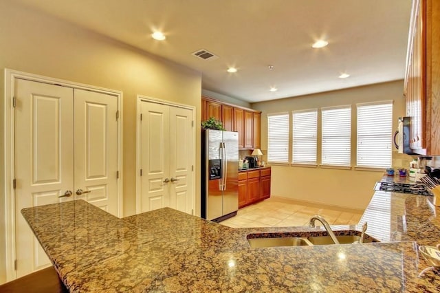 kitchen with kitchen peninsula, appliances with stainless steel finishes, stone counters, and sink