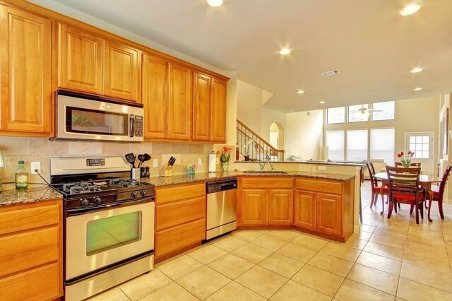 kitchen with kitchen peninsula, light tile patterned floors, stainless steel appliances, and light stone counters