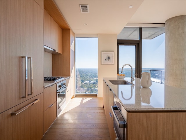 kitchen with visible vents, modern cabinets, light stone counters, stainless steel oven, and a sink