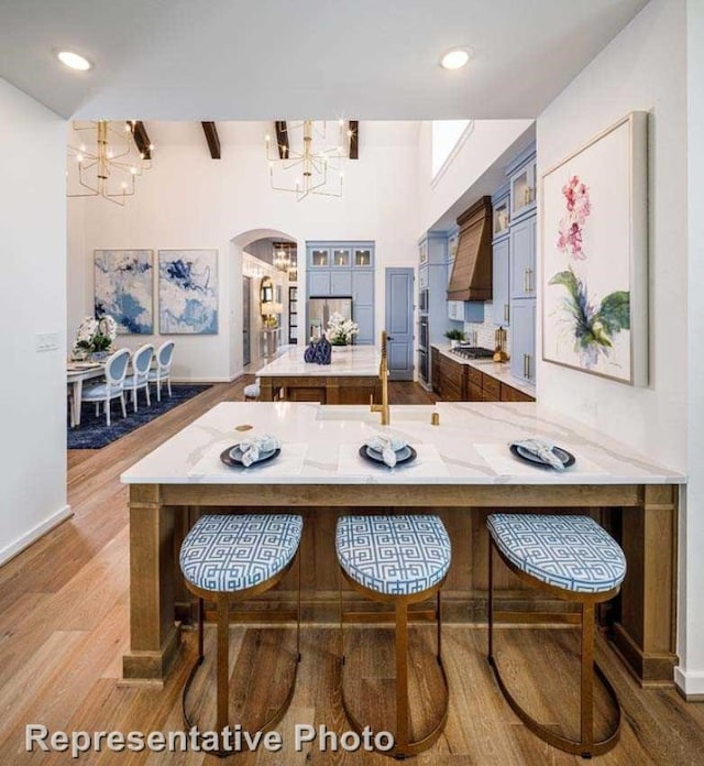 kitchen featuring hardwood / wood-style floors, custom exhaust hood, an inviting chandelier, kitchen peninsula, and stainless steel appliances