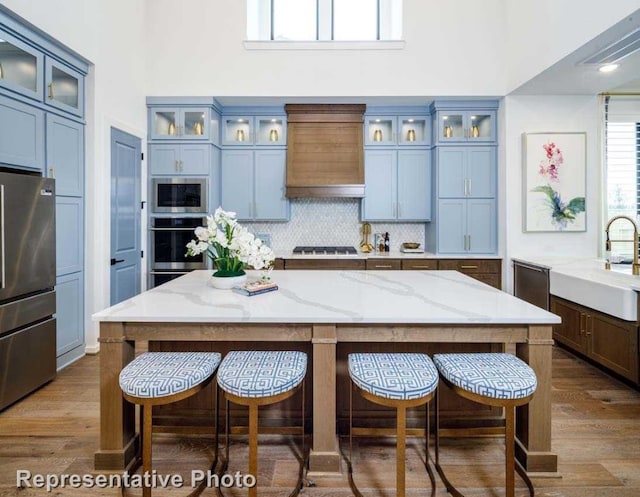 kitchen featuring appliances with stainless steel finishes, premium range hood, light stone counters, sink, and hardwood / wood-style floors