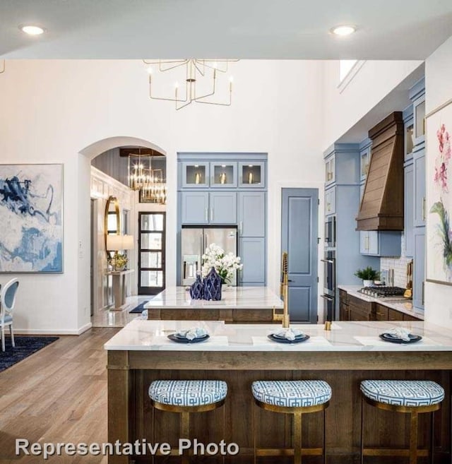 kitchen featuring premium range hood, wood-type flooring, decorative light fixtures, a kitchen bar, and appliances with stainless steel finishes