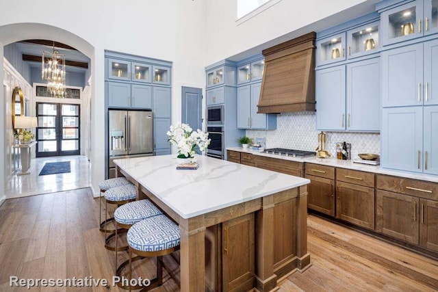 kitchen featuring custom exhaust hood, light hardwood / wood-style flooring, light stone countertops, appliances with stainless steel finishes, and a kitchen island