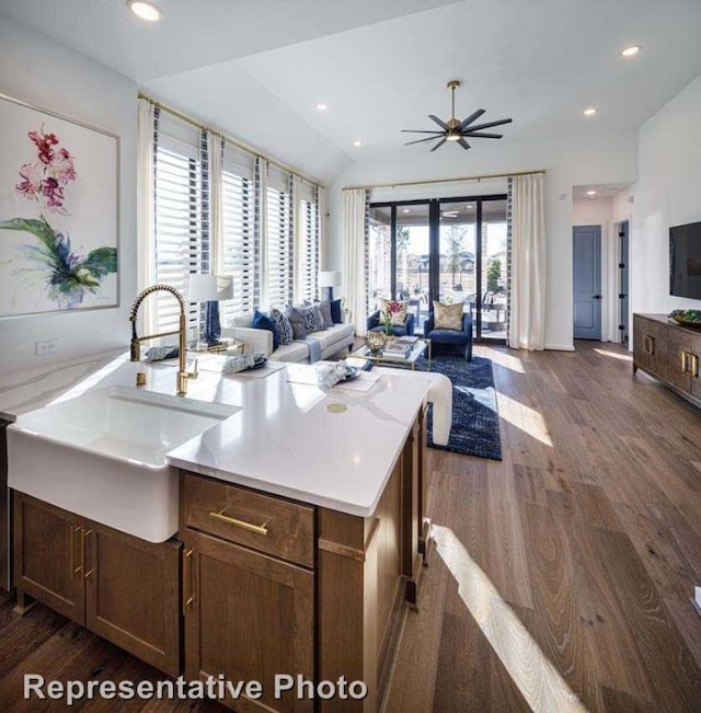 kitchen with ceiling fan, sink, dark wood-type flooring, vaulted ceiling, and a kitchen island with sink