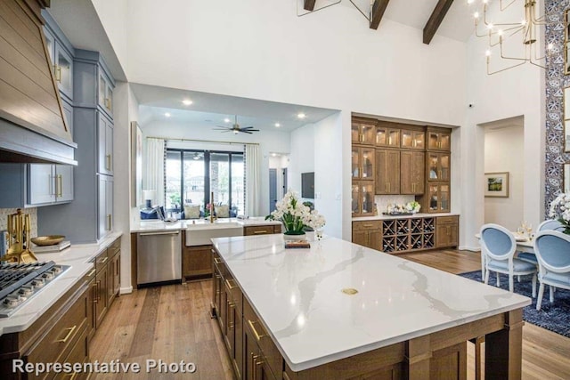 kitchen featuring a spacious island, light stone countertops, light wood-type flooring, appliances with stainless steel finishes, and beamed ceiling