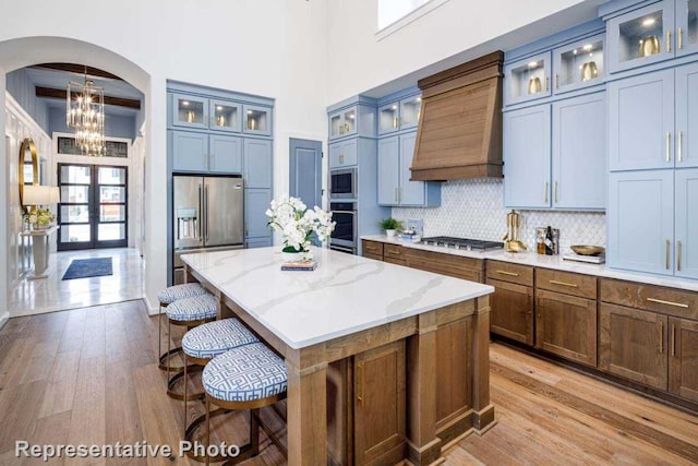 kitchen with arched walkways, stainless steel appliances, custom range hood, a kitchen breakfast bar, and a center island