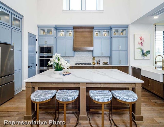 kitchen featuring backsplash, a breakfast bar, custom exhaust hood, stainless steel appliances, and a sink