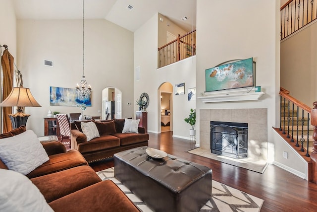 living room with high vaulted ceiling, hardwood / wood-style floors, a tiled fireplace, and an inviting chandelier