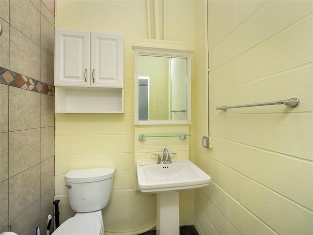 bathroom featuring toilet, sink, and tile walls