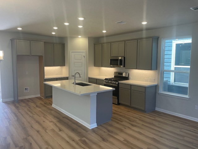 kitchen with gray cabinetry, sink, dark wood-type flooring, an island with sink, and appliances with stainless steel finishes