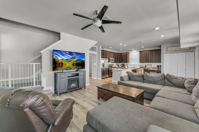 living room with a textured ceiling, ceiling fan, light hardwood / wood-style floors, and a fireplace