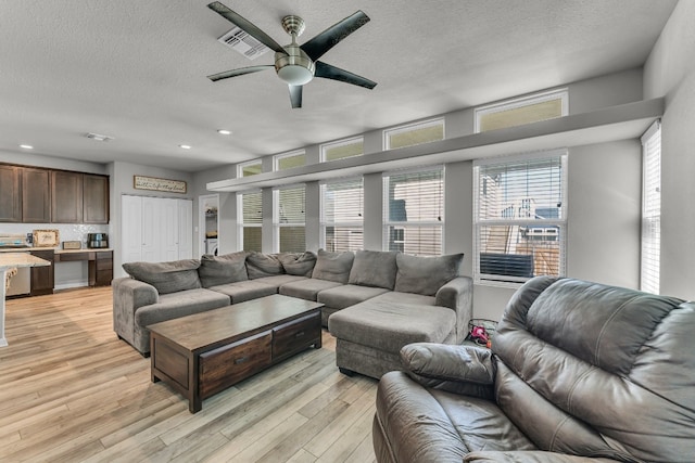 living room with a textured ceiling, light wood-type flooring, and ceiling fan