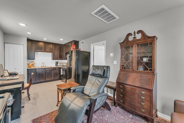 kitchen featuring stainless steel range, tasteful backsplash, black refrigerator, light tile patterned floors, and dark brown cabinets