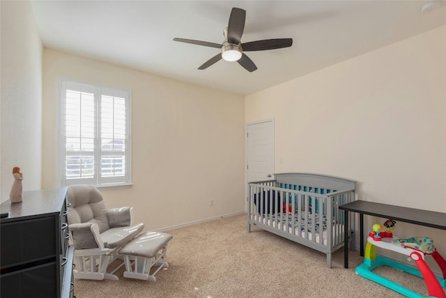 bedroom with a crib, light colored carpet, and ceiling fan