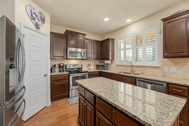 kitchen with sink, tasteful backsplash, appliances with stainless steel finishes, a kitchen island, and light hardwood / wood-style floors