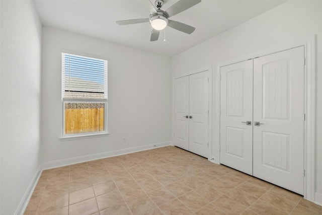 unfurnished bedroom with light tile patterned floors, ceiling fan, and multiple closets