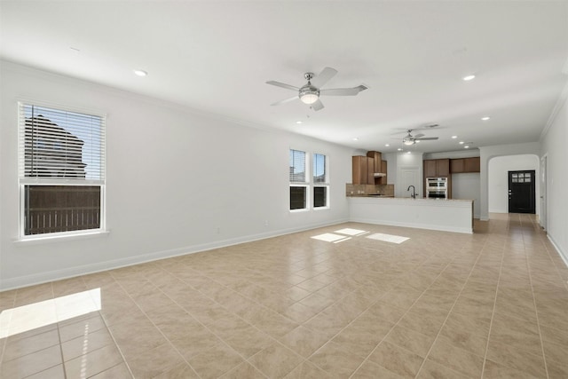 unfurnished living room featuring ceiling fan, sink, light tile patterned floors, and crown molding