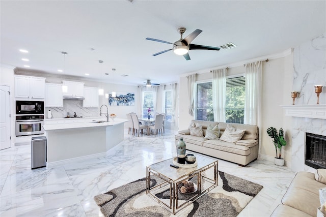 living room featuring ceiling fan, crown molding, a premium fireplace, and sink